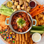 round board with pot of chili in center, surrounded by game day snacks