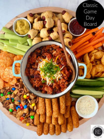 chili in the center of a game day board with cheese sticks, veggies, dips, chips