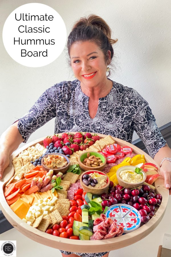 woman holding a round big board with hummus