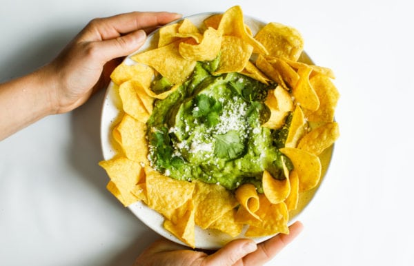 holding a plate of Best Avocado Salsa Verde with chips