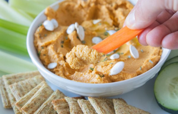 dipping carrot into pumpkin hummus