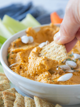 dipping Triscuit cracker into pumpkin hummus