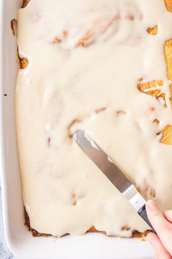 adding the frosting to cinnamon roll cake