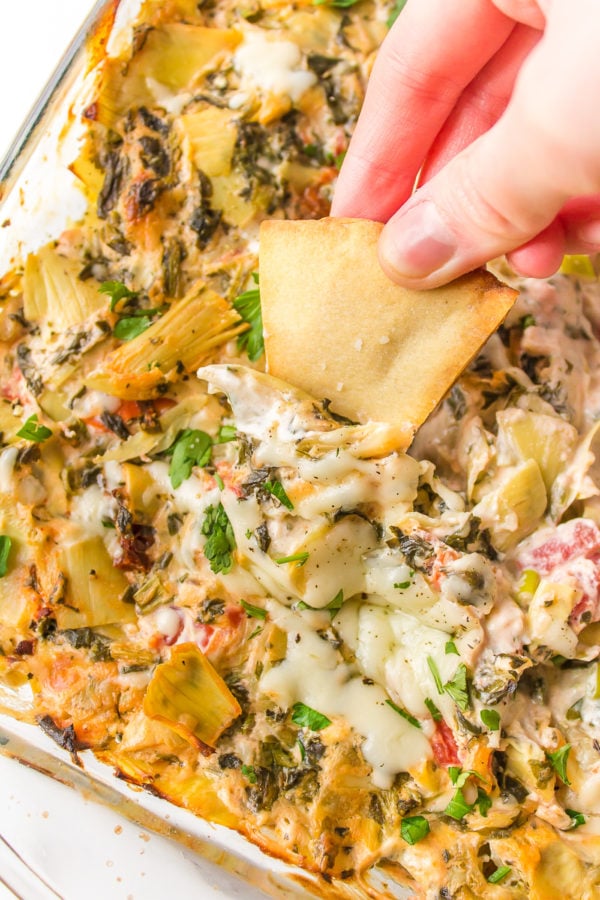 dipping pita chips into Cake Pan Artichoke Dip