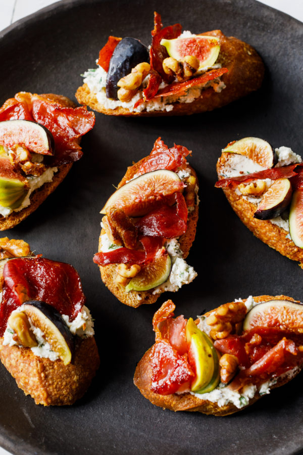 black plate of crostini with goat cheese and figs