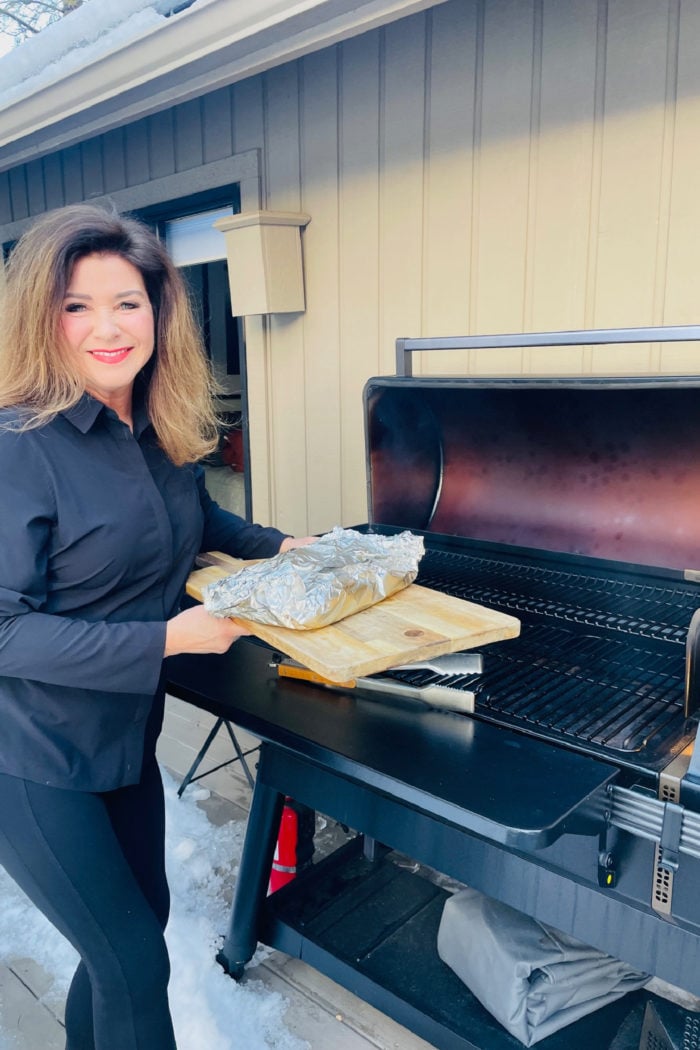 woman smoking a brisket wrapped in foil on a Traeger grill