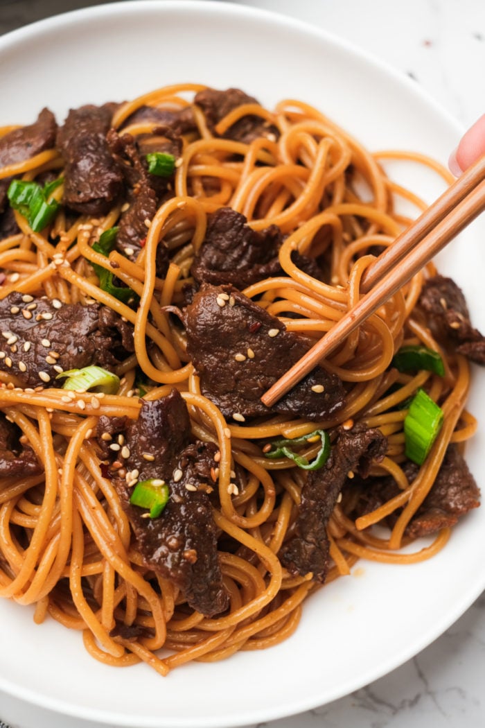 taking a bite of beef and noodles