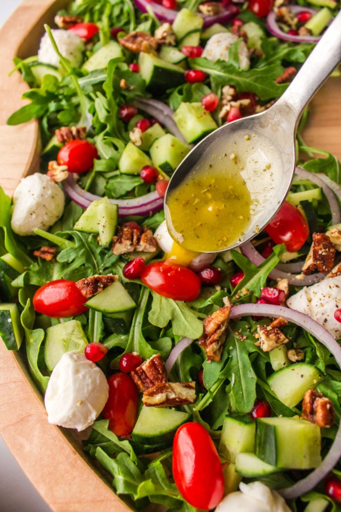 spooning dressing on arugula salad