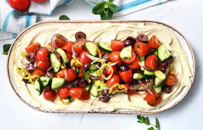 adding Greek salad ingredients to hummus