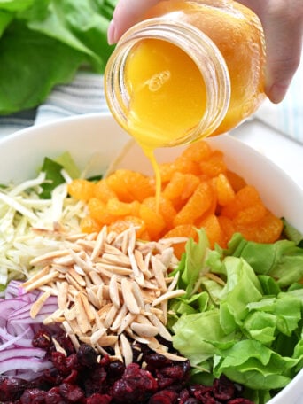 pouring orange salad dressing over a green salad