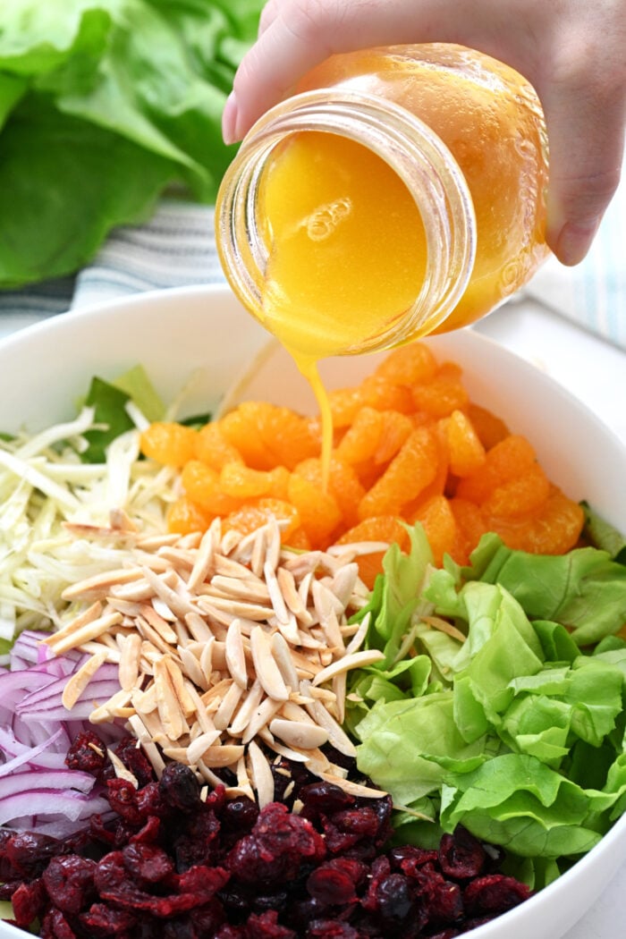 pouring orange salad dressing over a green salad