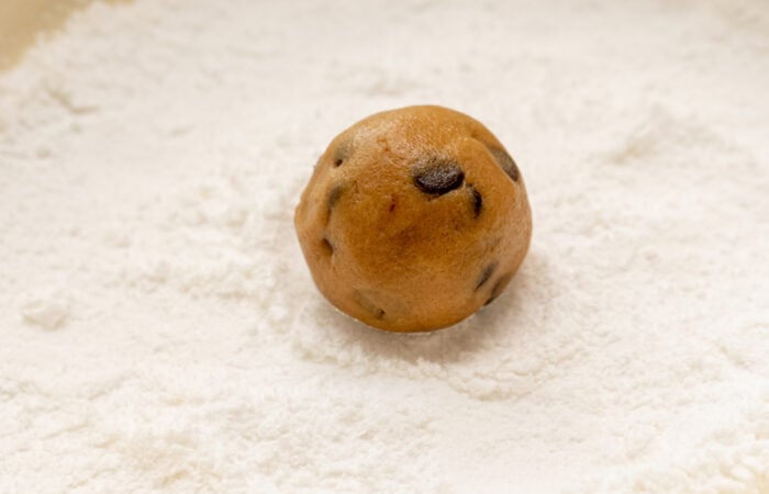 rolling a chocolate chip cookie in powdered sugar