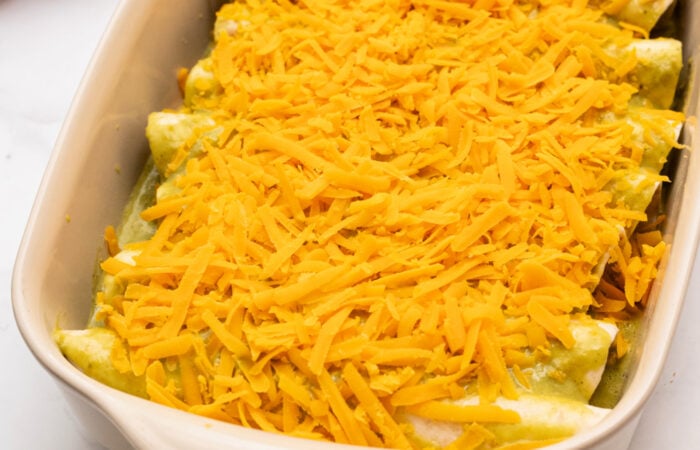 adding shredded cheese to enchiladas