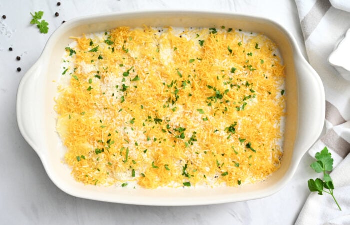 adding cheese on top of sliced potatoes for scalloped potatoes