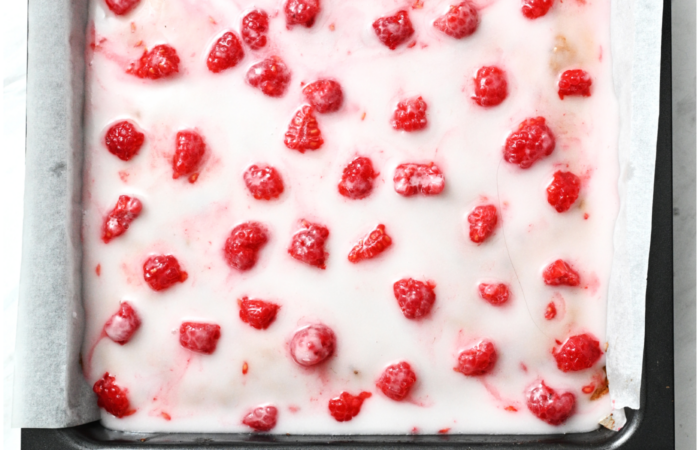 adding frosting and raspberries to cake