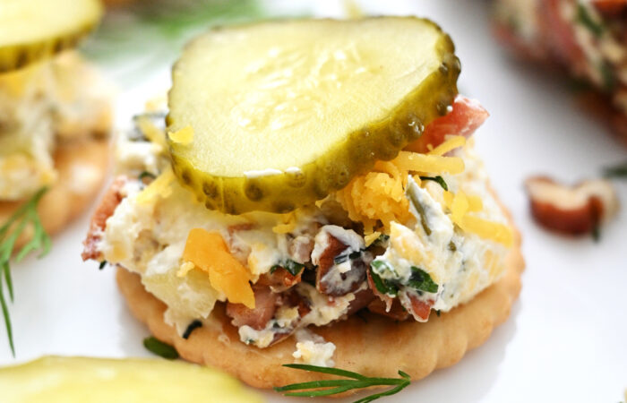cheese ball on cracker with a slice of pickle